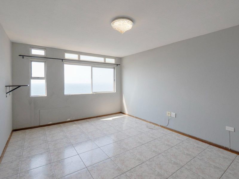 An empty bedroom featuring tiled flooring, neutral walls, and a large window with ocean views, ready for personalization.