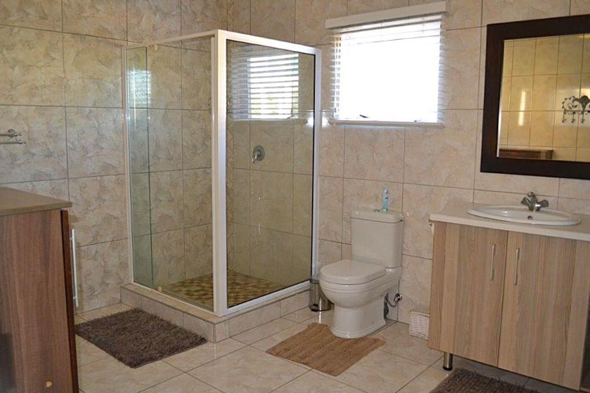 A functional bathroom featuring a glass shower enclosure, a vanity unit with a basin, and a toilet, finished with neutral wall and floor tiles.
