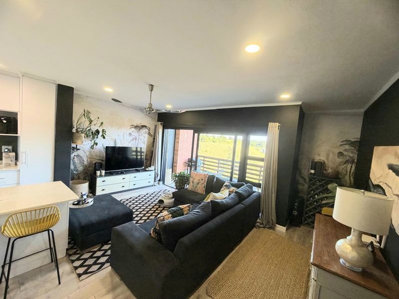 An open-plan living area featuring a kitchen island, recessed lighting, and large sliding glass doors that open to a balcony with scenic views.