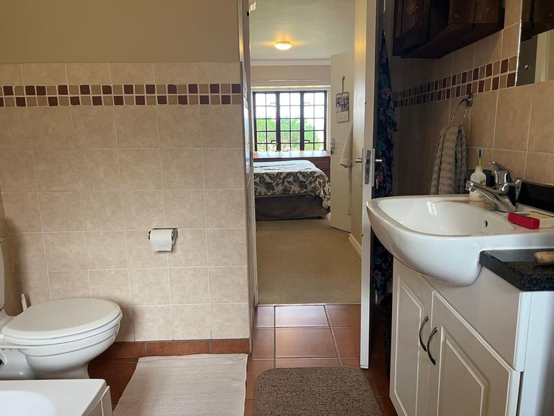 A functional bathroom featuring tiled walls and floors, a vanity with a basin, and a toilet, with a view into the adjacent bedroom.