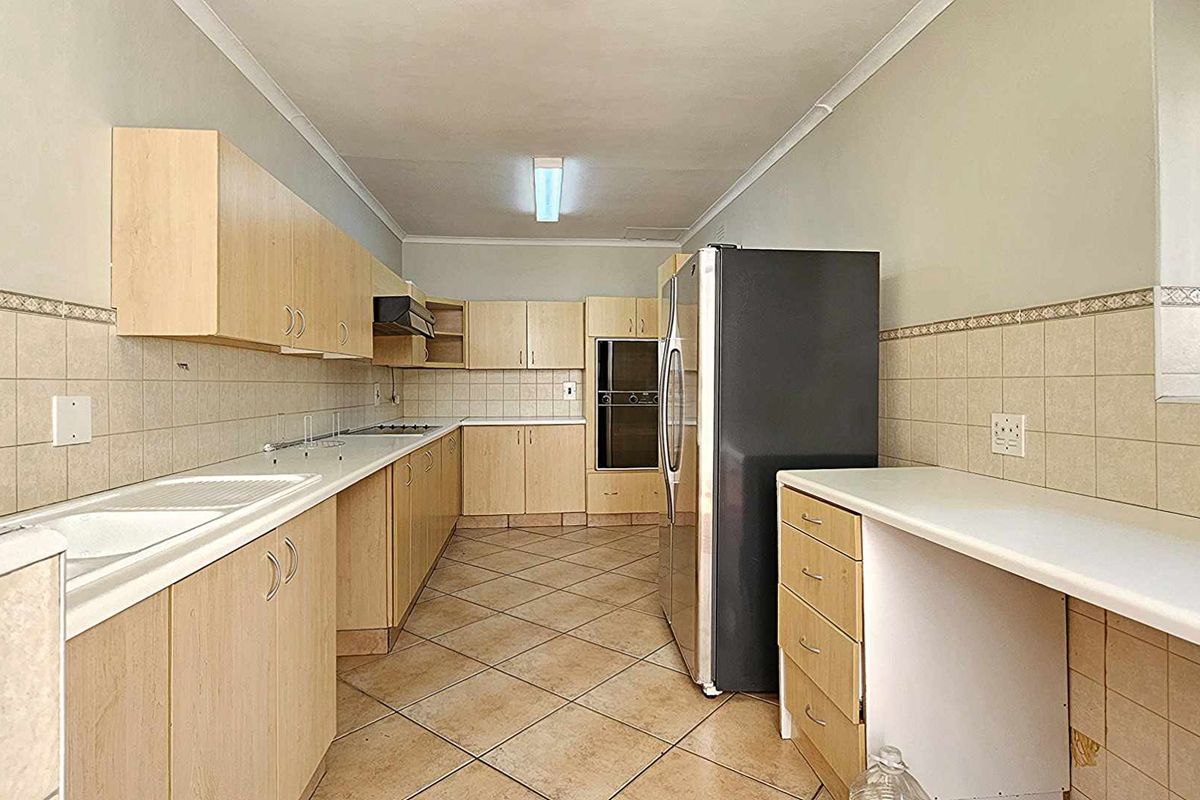 A functional galley-style kitchen featuring light wood cabinetry, tiled flooring, a built-in oven, and ample counter space for meal preparation.