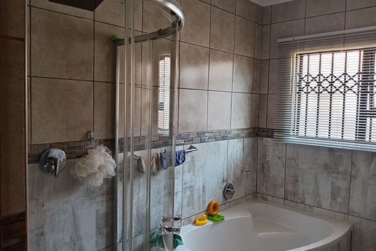 A functional bathroom featuring a corner bathtub, a glass-enclosed shower with a rainfall showerhead, and neutral wall tiling.