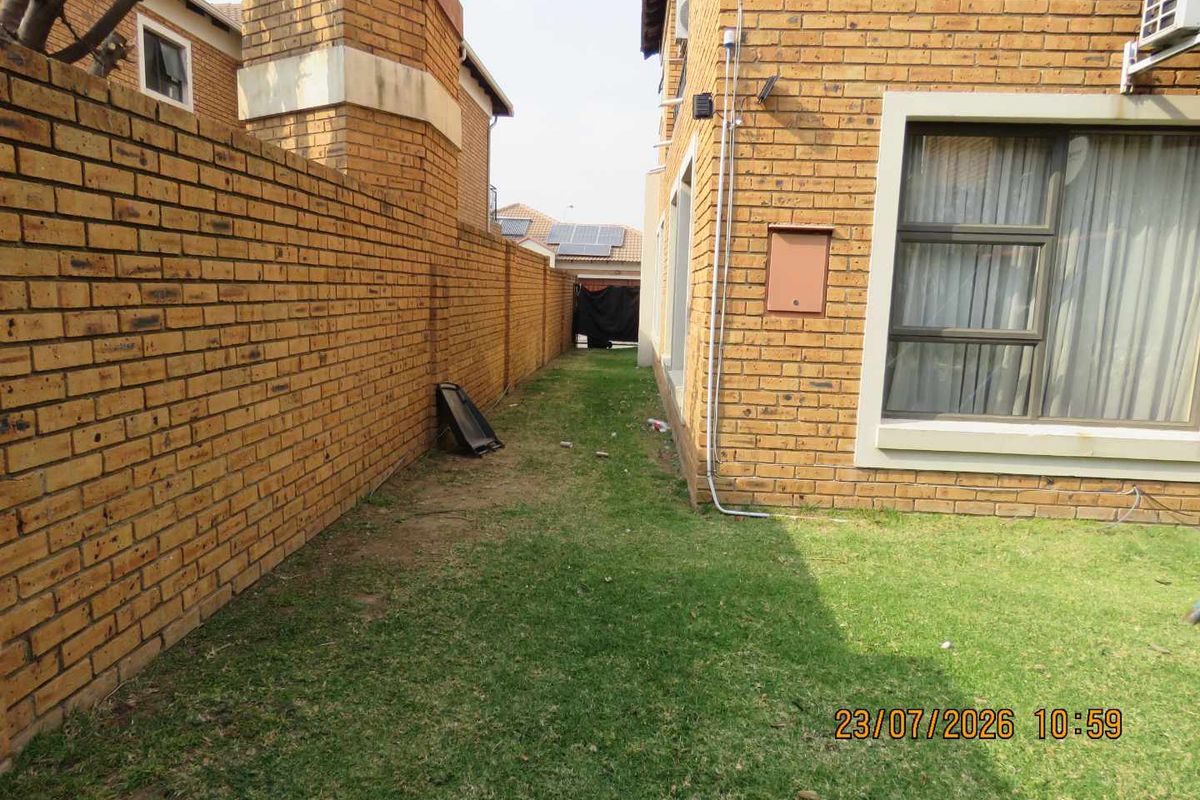 A side garden area featuring a face brick boundary wall and exterior facade with aluminum window frames and an installed air conditioning unit.