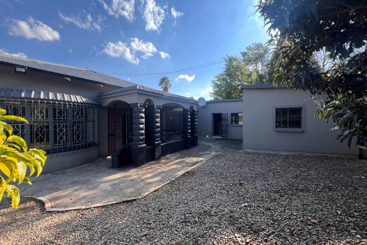 Rear view of the property featuring a concrete patio area, gravel yard, and secure metal window bars.