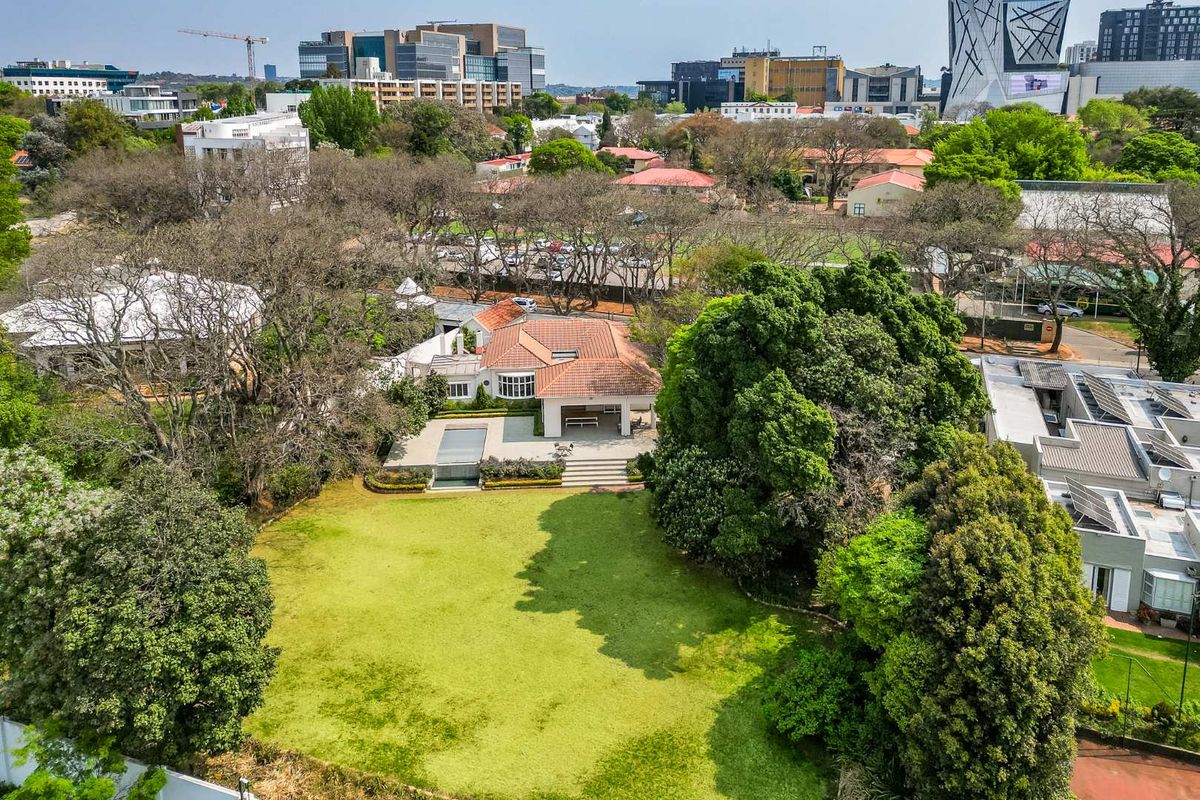 Aerial view of a residential property featuring a large garden, swimming pool, and a house with terracotta roof tiles in an urban setting.