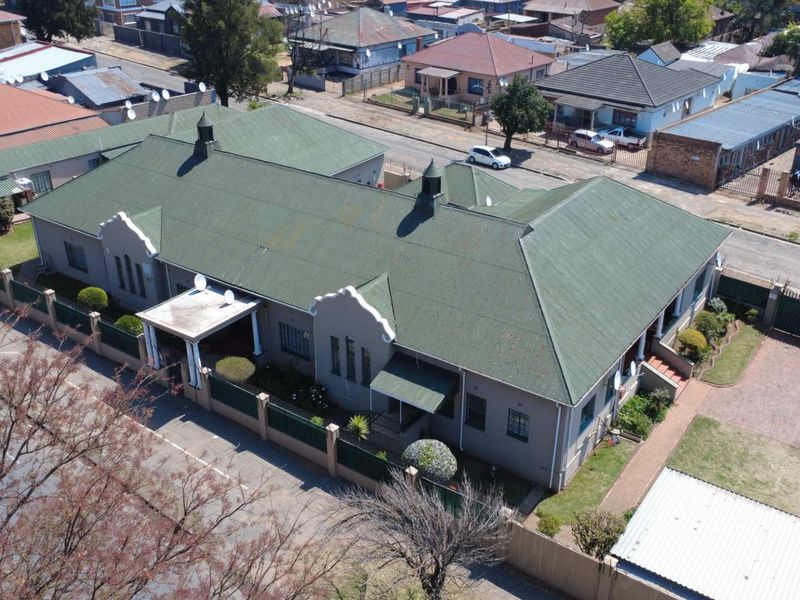Aerial view of a residential property featuring a large corrugated metal roof, perimeter walling, and a paved driveway in a suburban setting.