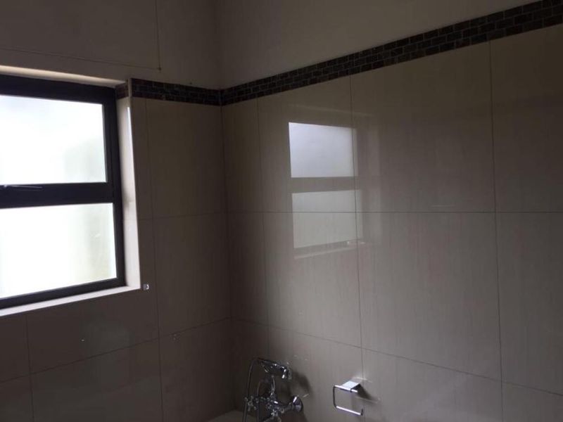 A clean bathroom featuring neutral wall tiles with a decorative mosaic border, chrome fixtures, and an aluminium-framed window.