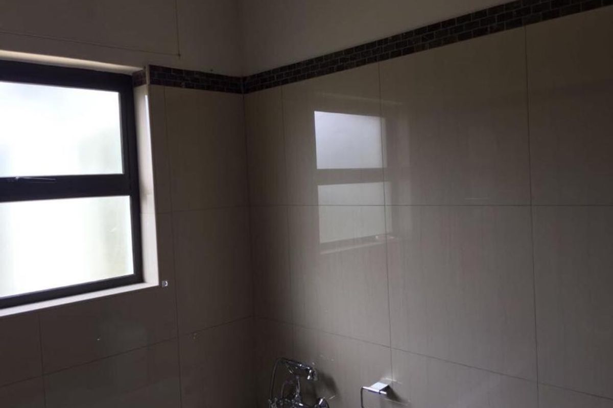 A clean bathroom featuring neutral wall tiles with a decorative mosaic border, chrome fixtures, and an aluminium-framed window.