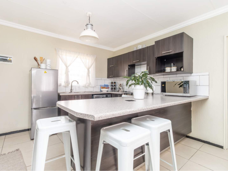A functional kitchen featuring dark wood cabinetry, a breakfast bar with laminate countertops, subway tile backsplash, and tiled flooring.