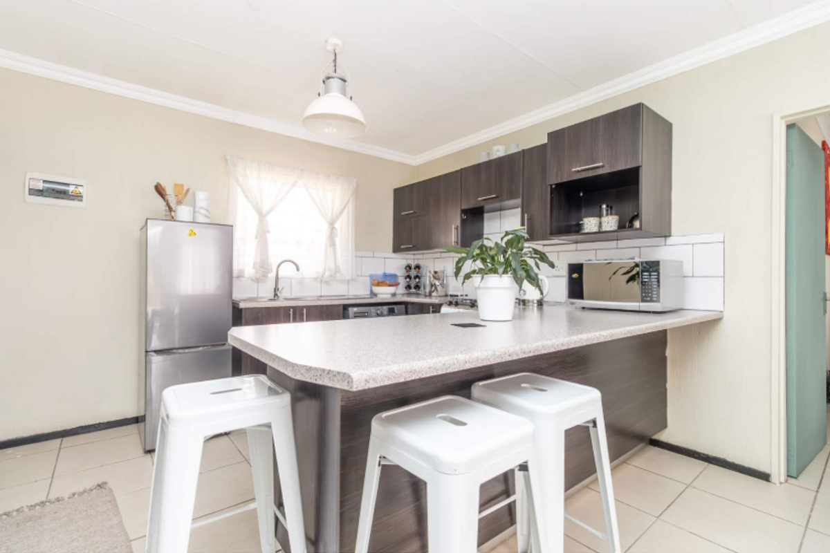 A functional kitchen featuring dark wood cabinetry, a breakfast bar with laminate countertops, subway tile backsplash, and tiled flooring.