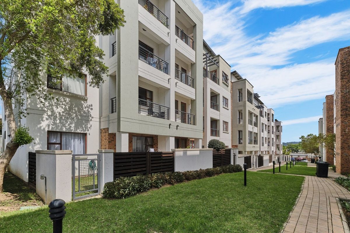 A view of the apartment complex exterior featuring multi-level balconies, paved walkways, and well-maintained communal garden areas.