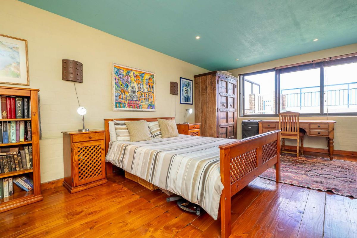 A bedroom featuring polished hardwood flooring, recessed ceiling lighting, and large windows providing natural light and access to an outdoor balcony area.