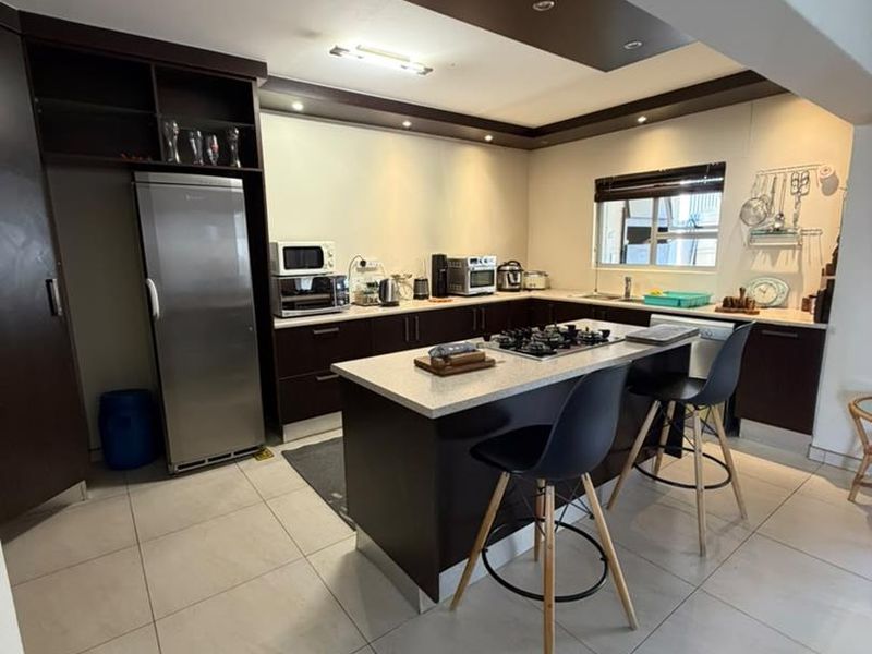 Modern kitchen featuring a central island with a gas cooktop, dark cabinetry, stone countertops, and recessed lighting, providing a functional and contemporary cooking space.