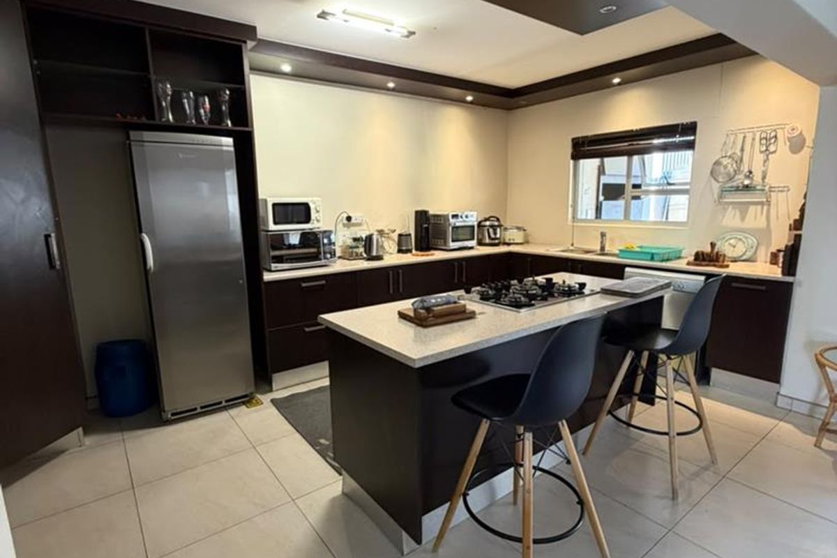 Modern kitchen featuring a central island with a gas cooktop, dark cabinetry, stone countertops, and recessed lighting, providing a functional and contemporary cooking space.