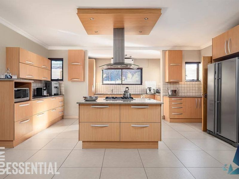 Spacious kitchen featuring light wood cabinetry, a central island with a gas hob, stone countertops, and modern stainless steel extractor fan.
