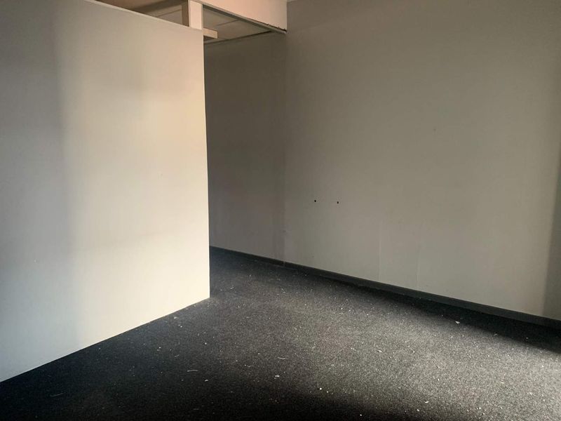 An empty office space featuring dark carpeting and a partition wall, requiring minor cosmetic updates to the ceiling and wall finishes.