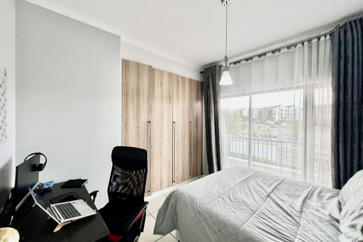 A well-maintained bedroom featuring built-in wooden cupboards, tiled flooring, and a sliding door providing access to a balcony with natural light.