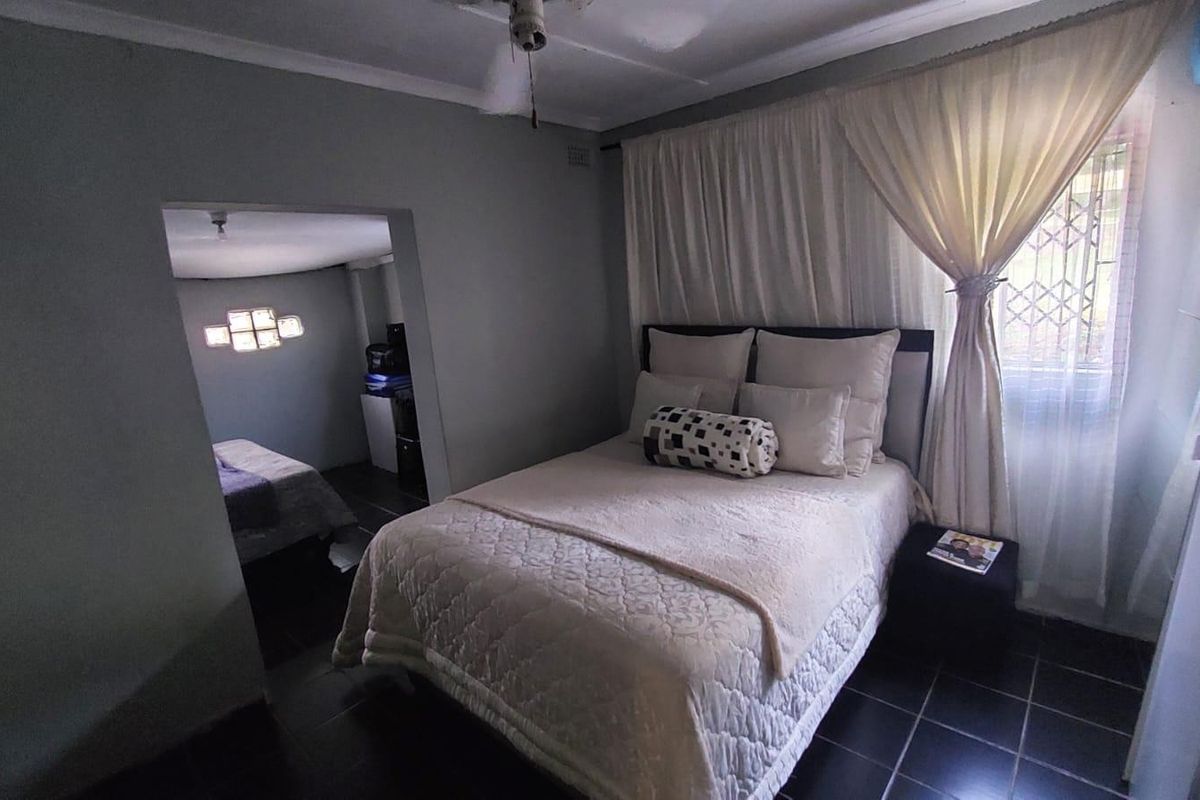 A bedroom featuring dark tiled flooring, a ceiling fan, and an adjoining room, with natural light filtered through window curtains.