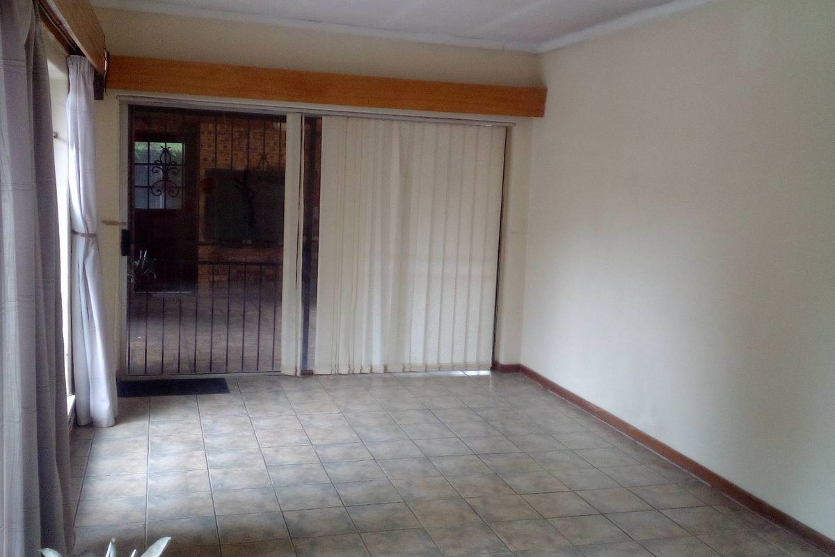 A spacious, empty living area featuring tiled flooring and a large sliding glass door with security gate leading to an outdoor space.