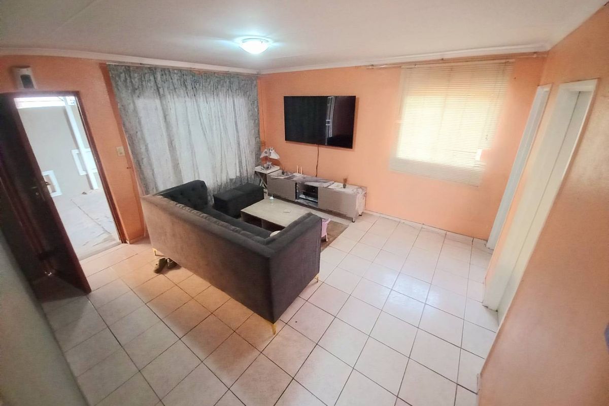 A living room featuring tiled flooring, peach-toned walls, and a ceiling-mounted light fixture, providing a functional and open living space.