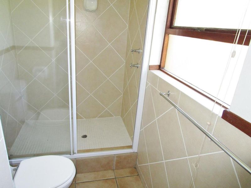 A functional bathroom featuring a shower enclosure with tiled walls, a toilet, and a window, presenting a dated but well-maintained space.