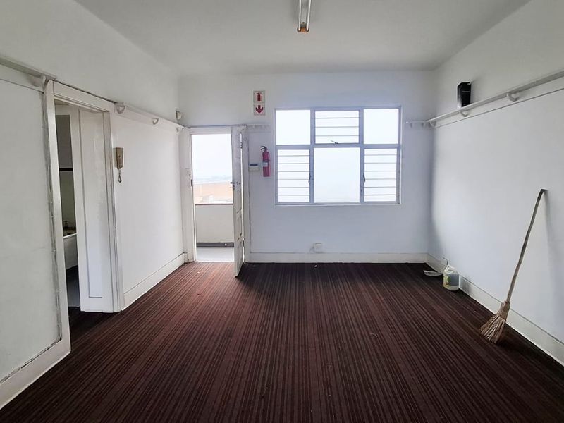 An empty office space featuring dark carpet flooring, picture rails, and a large window providing natural light and access to an adjacent balcony.