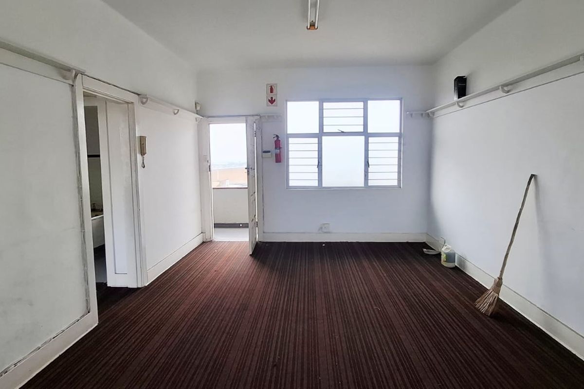 An empty office space featuring dark carpet flooring, picture rails, and a large window providing natural light and access to an adjacent balcony.
