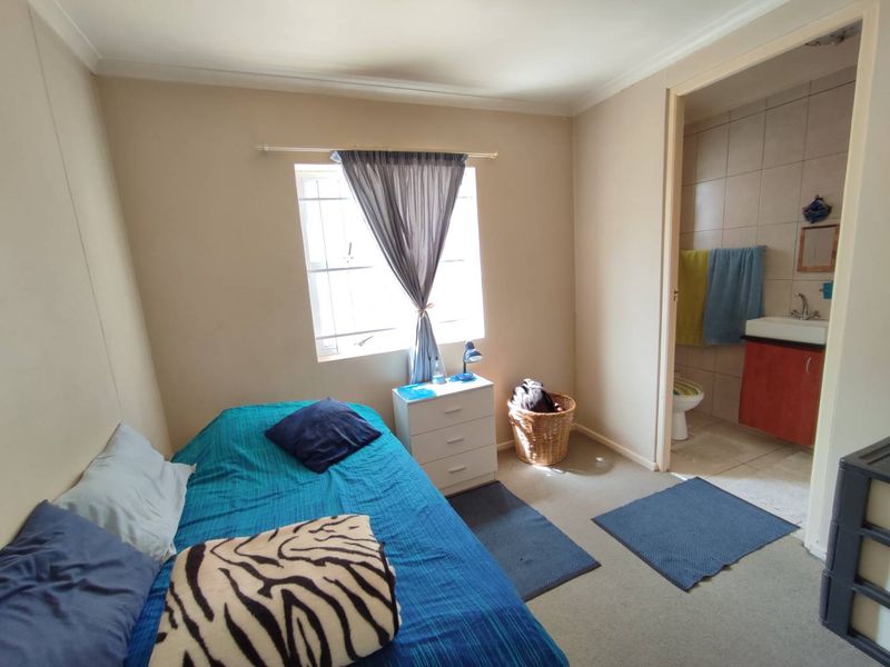 A functional bedroom featuring a window with security bars and an adjoining en-suite bathroom with a vanity and toilet.