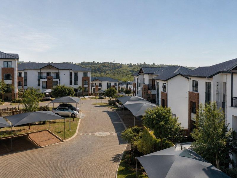 An elevated view of the apartment complex grounds, featuring paved driveways, designated shade cloth parking bays, and well-maintained residential building exteriors.