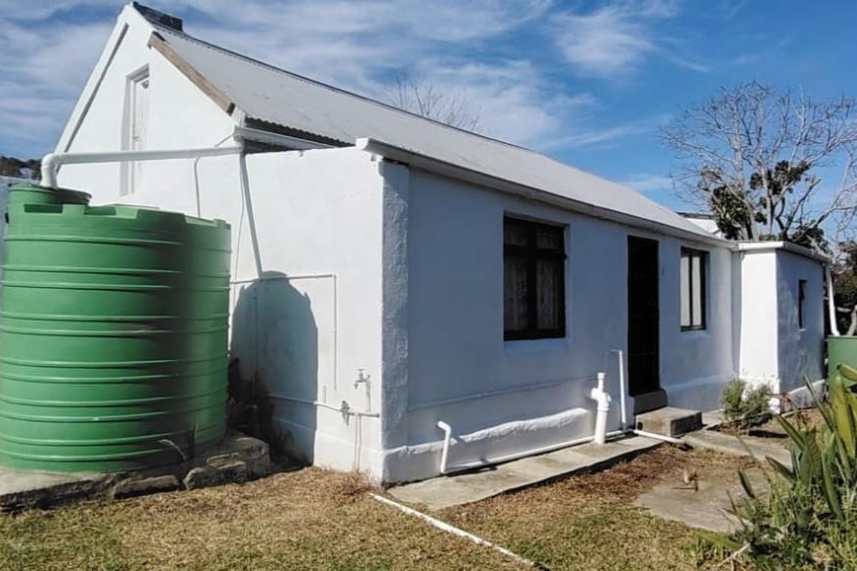 Rear view of the property featuring a white exterior, corrugated metal roof, and a large green rainwater storage tank.