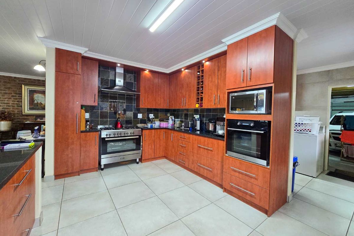 A functional kitchen featuring cherry wood cabinetry, dark stone countertops, a built-in oven, microwave, and a stainless steel extractor fan.