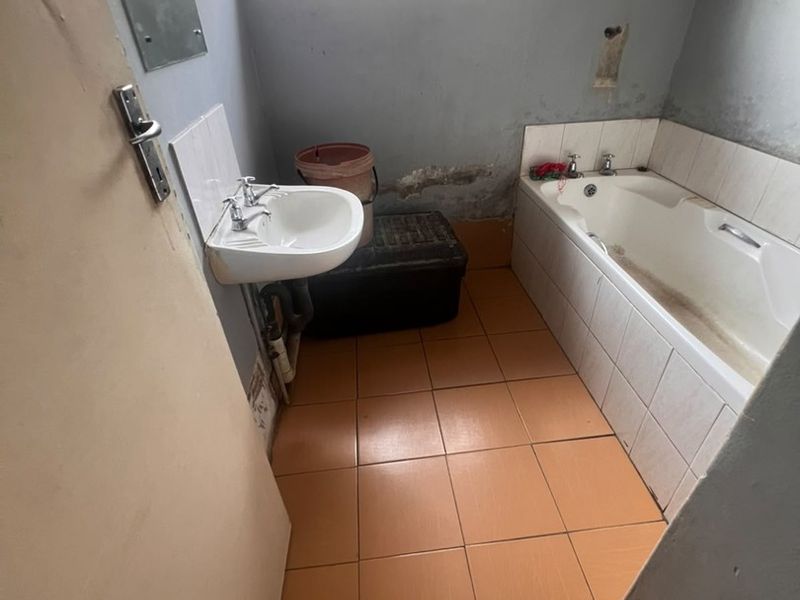A dated bathroom featuring a pedestal basin and built-in bathtub, requiring cosmetic updates and repairs to wall finishes.