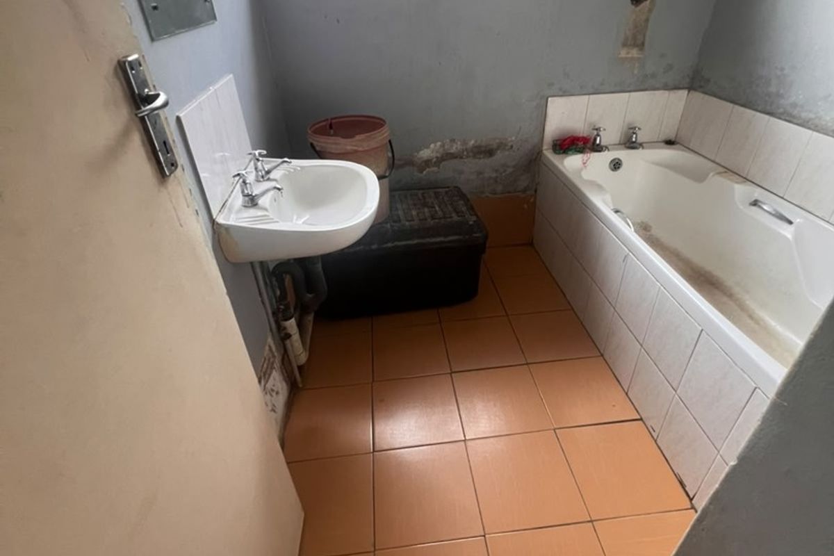 A dated bathroom featuring a pedestal basin and built-in bathtub, requiring cosmetic updates and repairs to wall finishes.