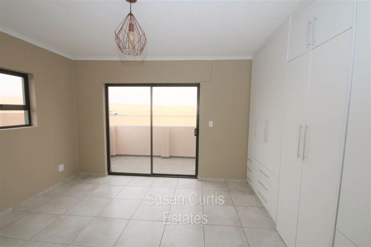 A bright bedroom featuring neutral tiled flooring, built-in white cabinetry, and sliding glass doors that open onto a private balcony.