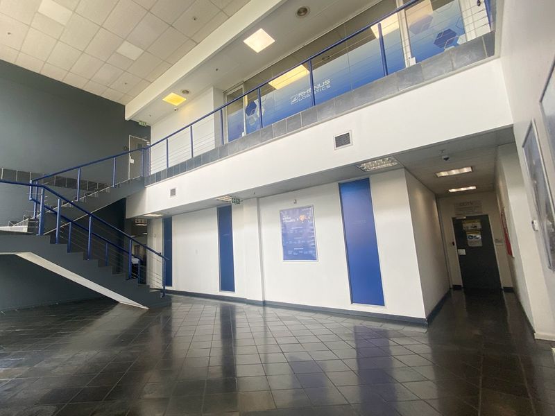 Spacious industrial entrance foyer featuring a double-volume ceiling, tiled flooring, and a mezzanine level with a metal staircase.