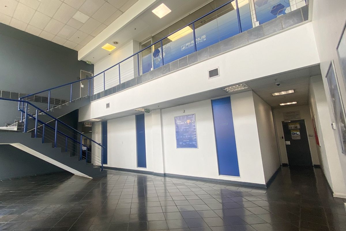 Spacious industrial entrance foyer featuring a double-volume ceiling, tiled flooring, and a mezzanine level with a metal staircase.