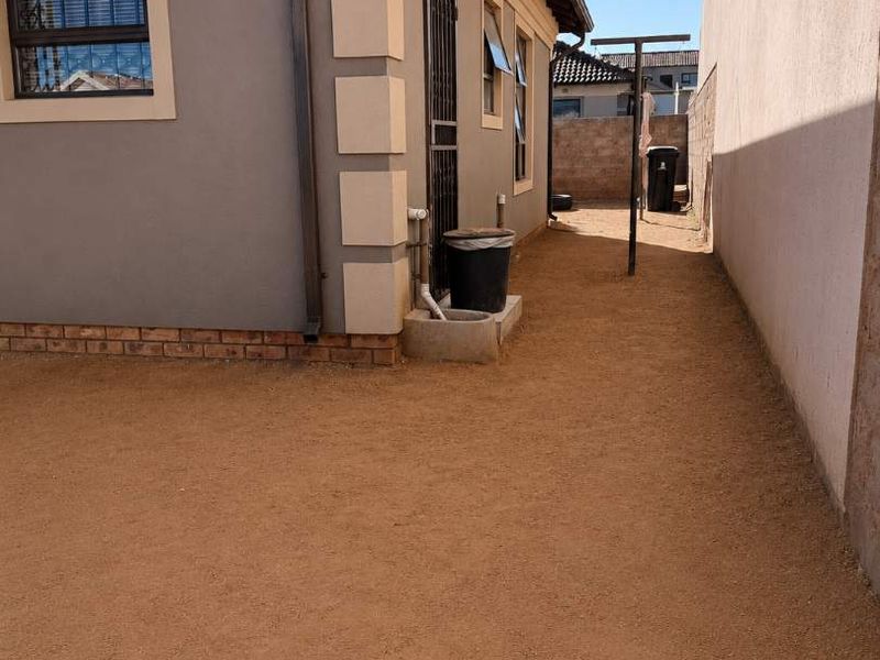 A view of the side and rear exterior of the house featuring a gravel ground surface, boundary wall, and security features.