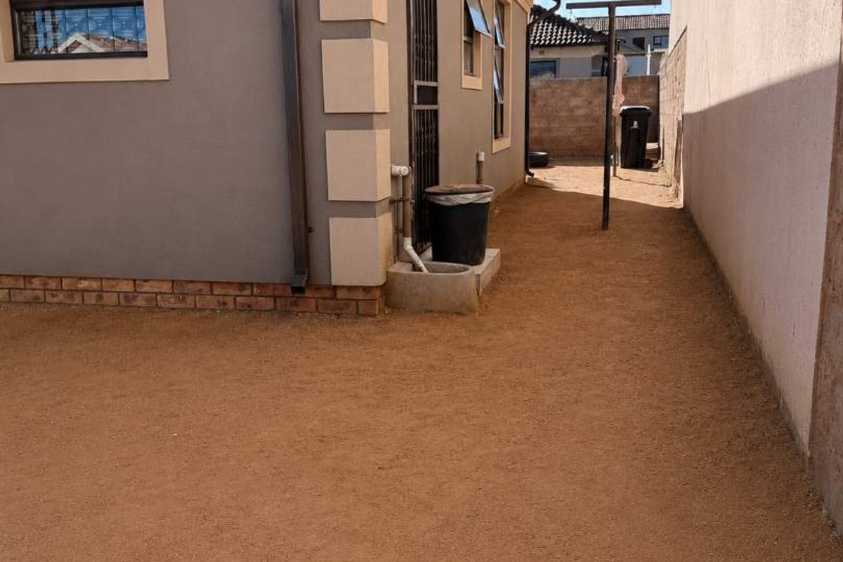 A view of the side and rear exterior of the house featuring a gravel ground surface, boundary wall, and security features.