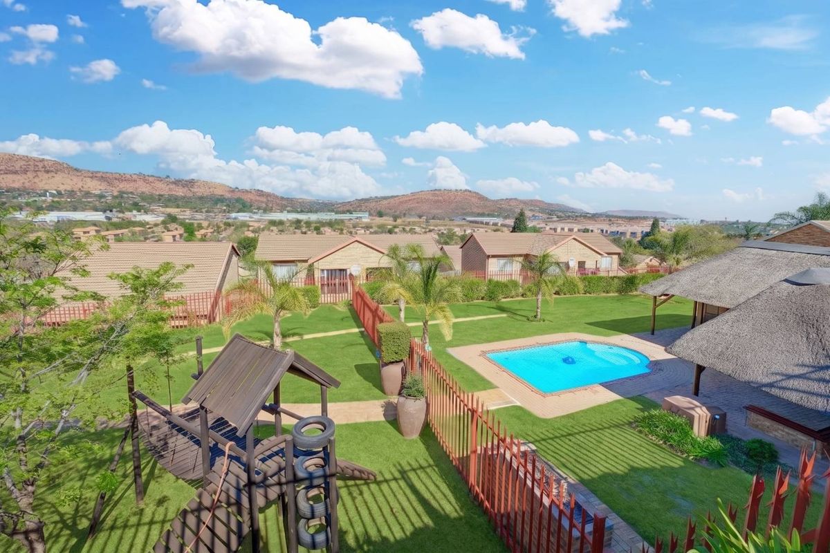 Elevated aerial view of a residential complex featuring a swimming pool, thatched lapa, landscaped garden, and surrounding townhouse properties.