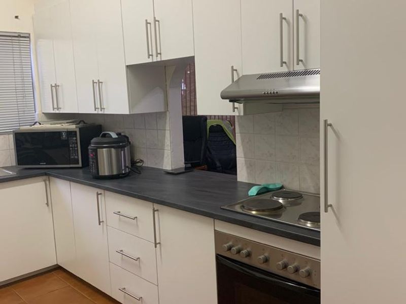 A functional kitchen featuring white cabinetry, dark laminate countertops, a built-in oven with electric hob, and an extractor fan.