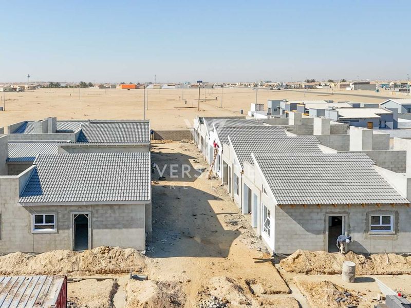 Aerial view of a townhouse development under construction, featuring concrete block structures, tiled roofs, and unfinished surrounding grounds.