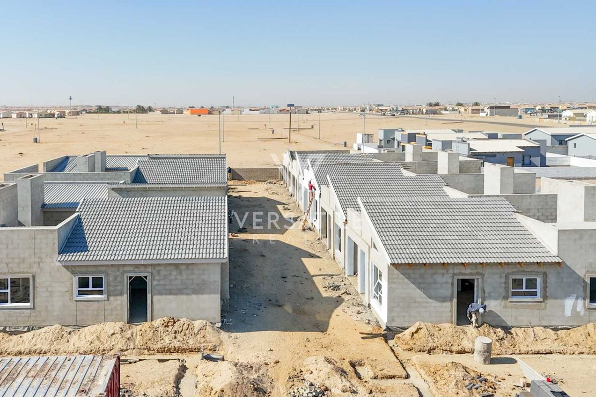 Aerial view of a townhouse development under construction, featuring concrete block structures, tiled roofs, and unfinished surrounding grounds.