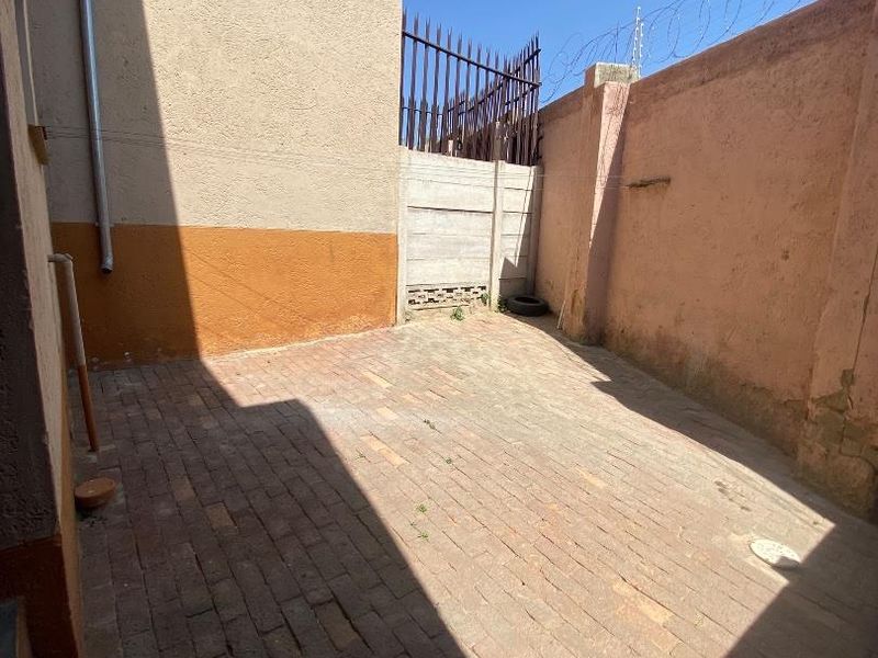 A private rear courtyard area featuring brick paving, enclosed by high perimeter walls with security fencing and razor wire.