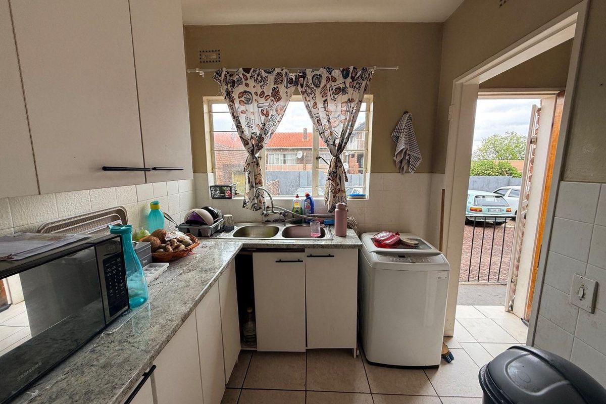 A functional kitchen area featuring laminate countertops, double basin sink, tiled backsplash, and direct access to the exterior through a security gate.