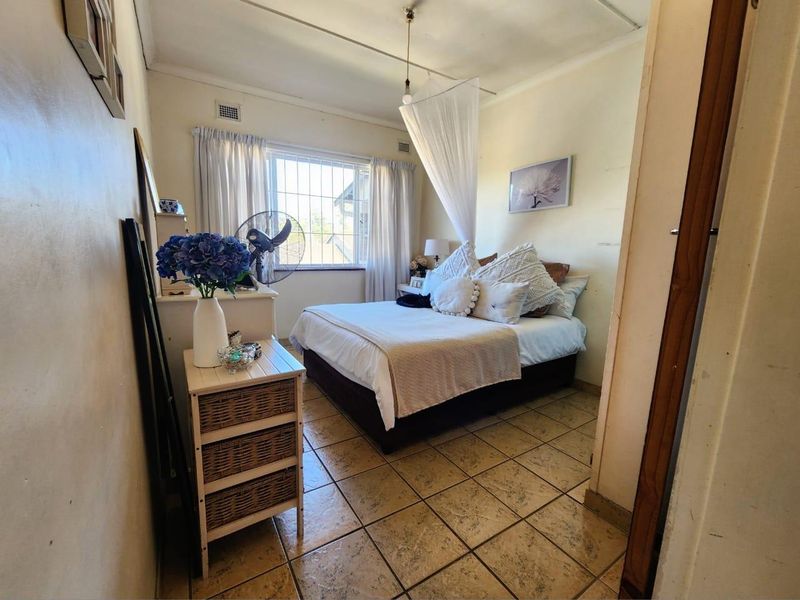 A compact bedroom featuring tiled flooring, a window with security bars, and a ceiling vent. The room requires cosmetic updates to the wall finishes.