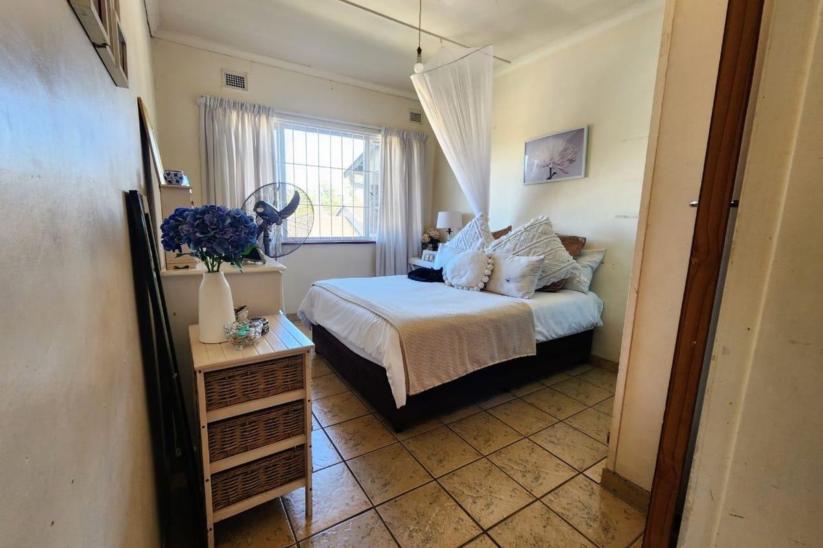 A compact bedroom featuring tiled flooring, a window with security bars, and a ceiling vent. The room requires cosmetic updates to the wall finishes.