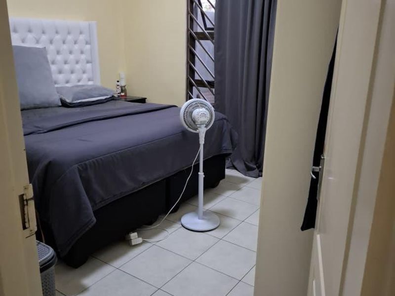 A functional bedroom featuring tiled flooring, a security gate on the window, and neutral wall finishes.