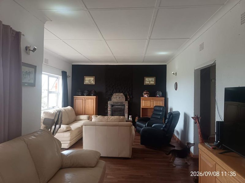 A living room featuring a central stone fireplace, laminate flooring, and a tiled ceiling, offering a functional and comfortable living space.