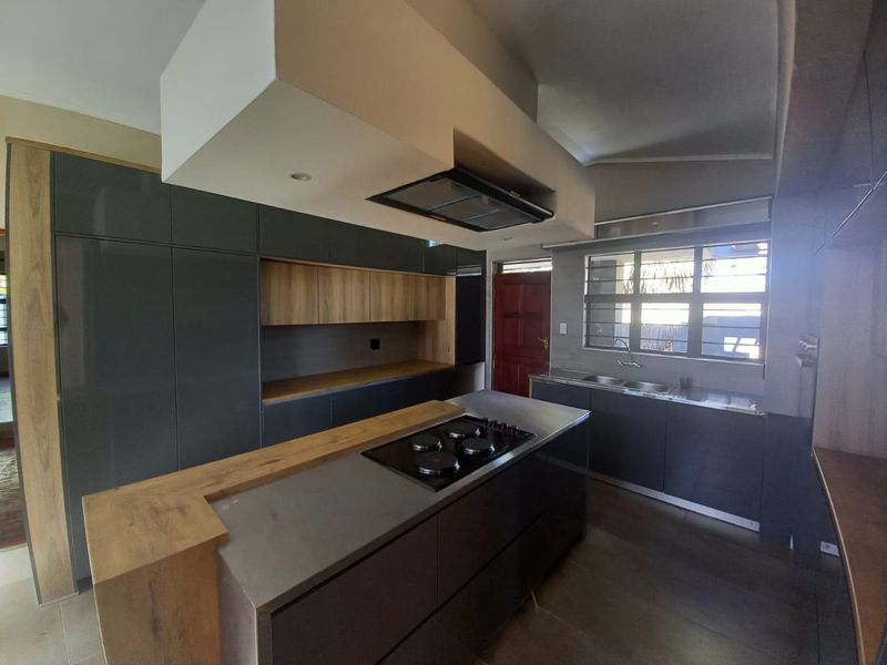 Modern kitchen featuring dark grey cabinetry, wood-look accents, a central island with a built-in hob, and a double sink under a window.
