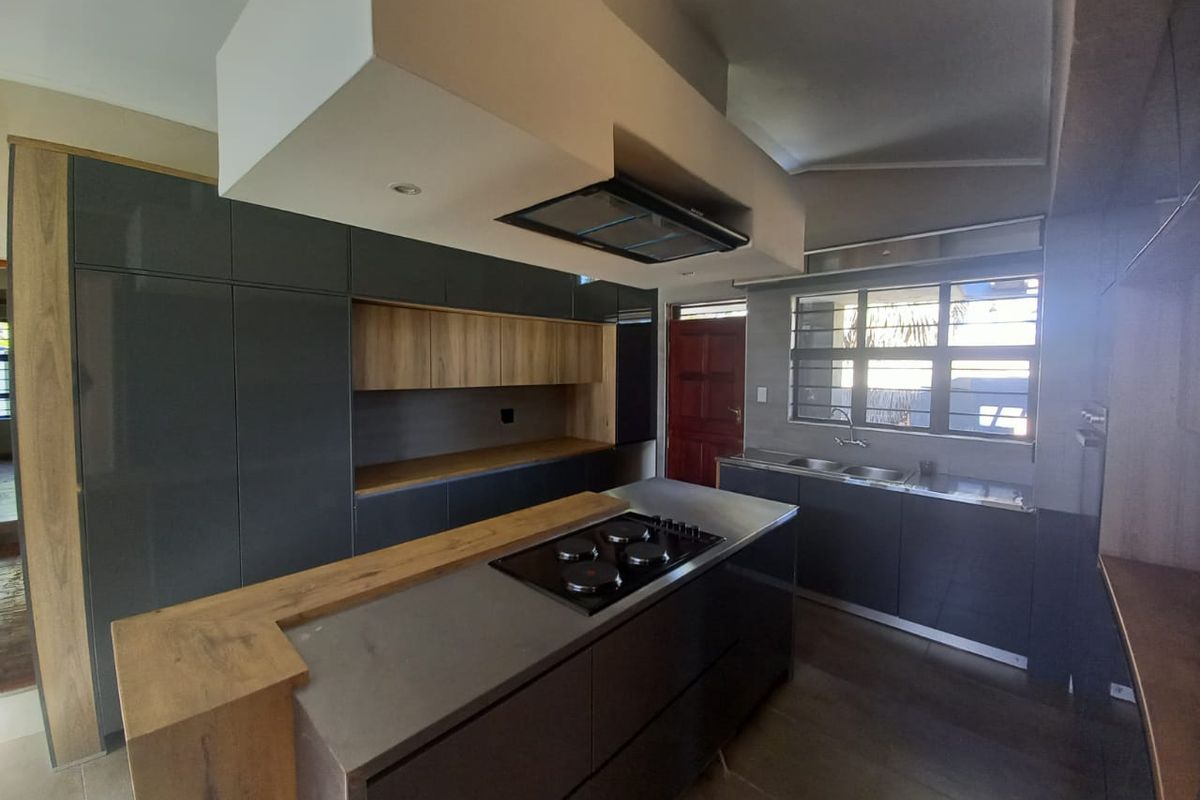 Modern kitchen featuring dark grey cabinetry, wood-look accents, a central island with a built-in hob, and a double sink under a window.